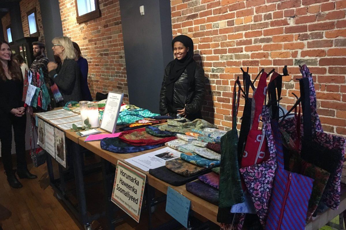 Photograph of a woman standing behind a table selling bags that she has hand-sewn herself.