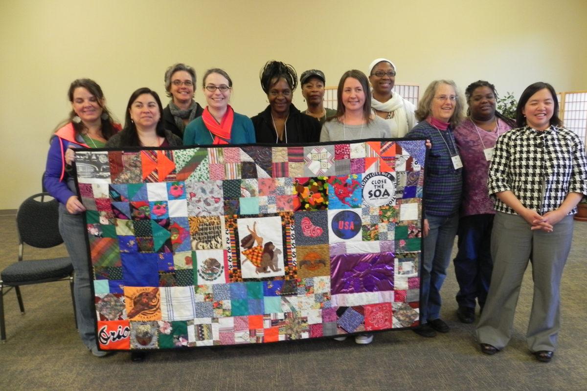 Photograph of a group of women holding a quilt with many different squares.
