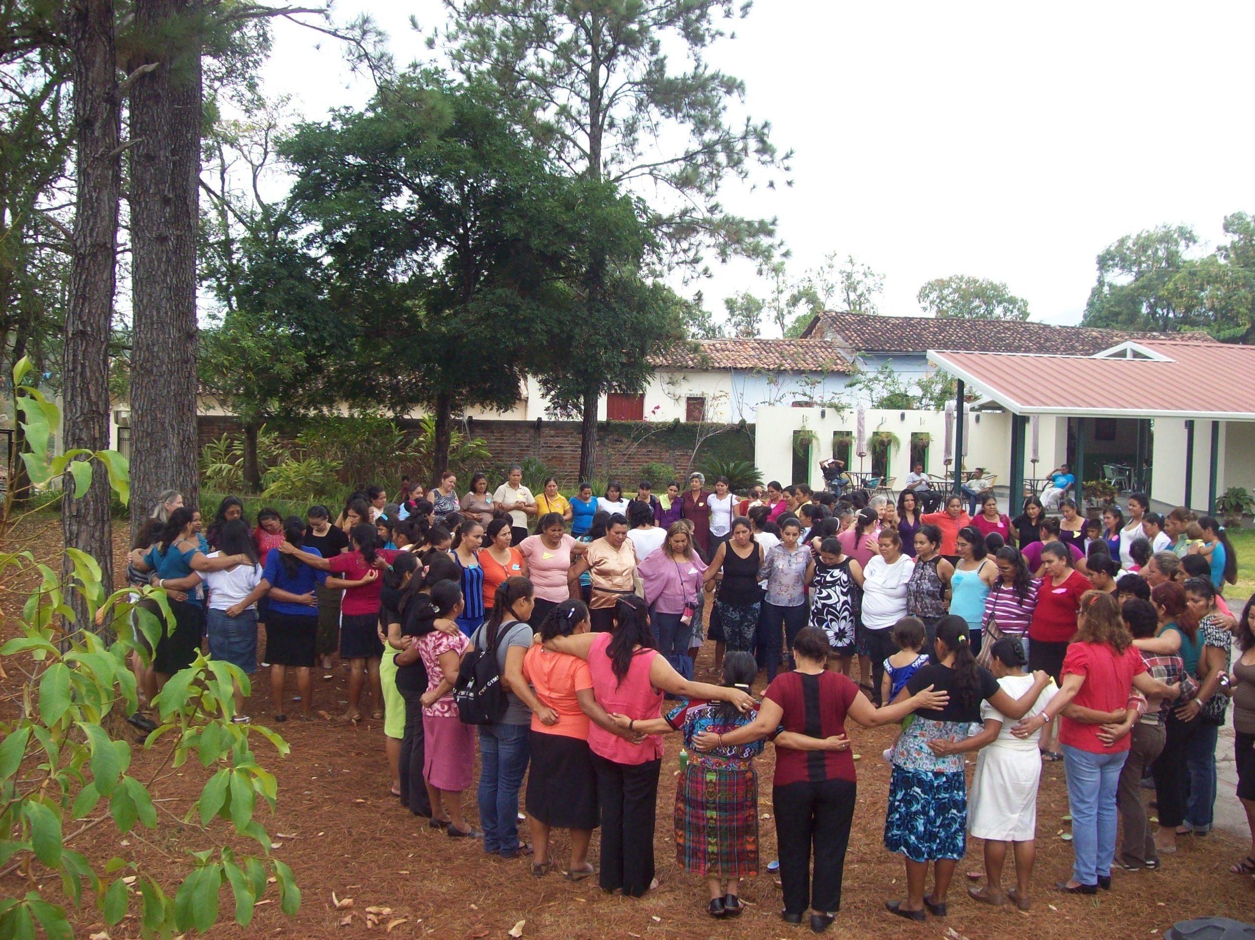 A large group of women standing outside in a circle wiht their arms around each other.