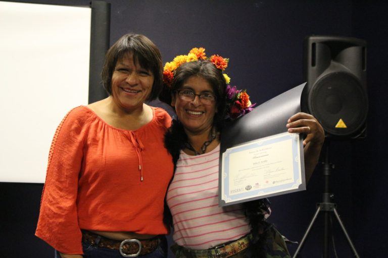 Photo of two latina women embracing, one woman holds up a diploma.