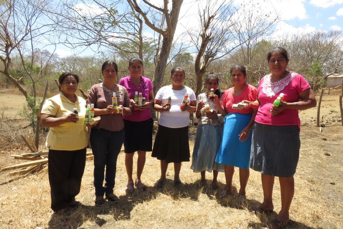 Group of women standing outside in a barren landscape in a semicircle holding up shampoos and soaps.