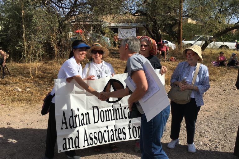 A woman shakes hands with another woman holding up a sign that says Adrian Dominicans and Associates for Peace