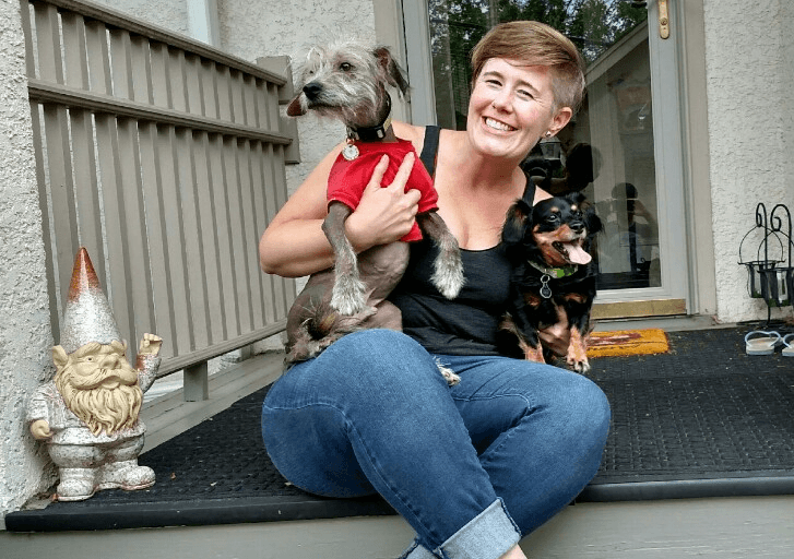 Robyn sitting on her front porch casually, smiling and holding her two small dogs.
