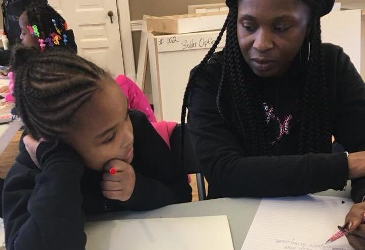 Photo of a black woman helping a young black girl on a writing project.