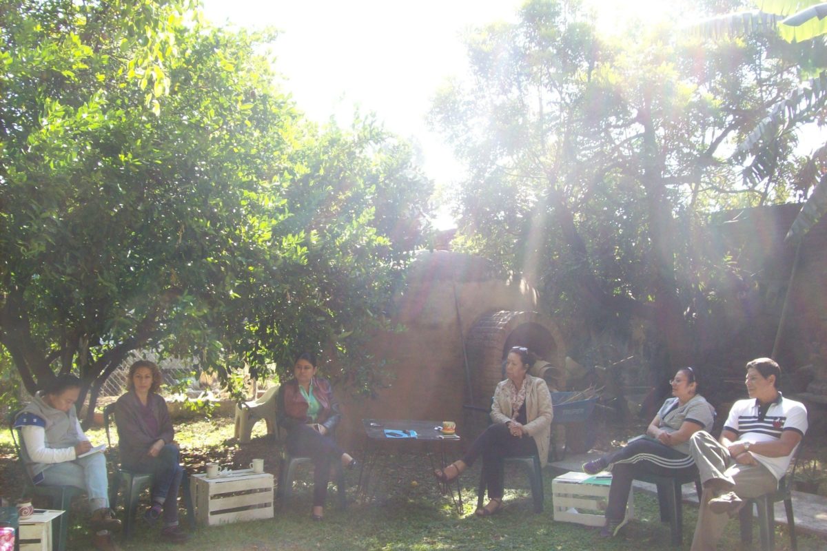 Several people sit outside on chairs with the Temazcal (steam bath) in the background.