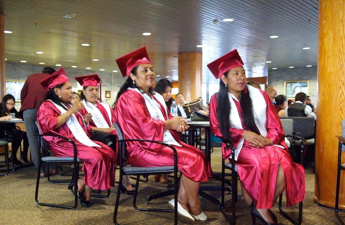 Photograph of several latina women in graduation caps and gowns sitting in rows.