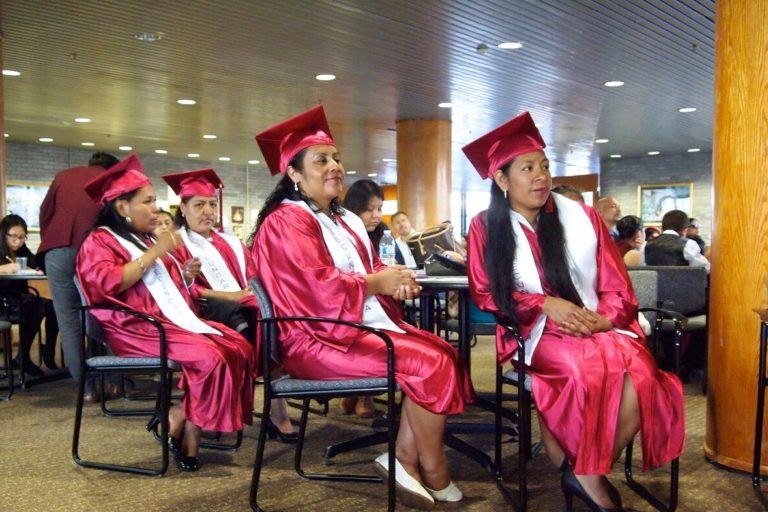 Photograph of several latina women in graduation caps and gowns sitting in rows.