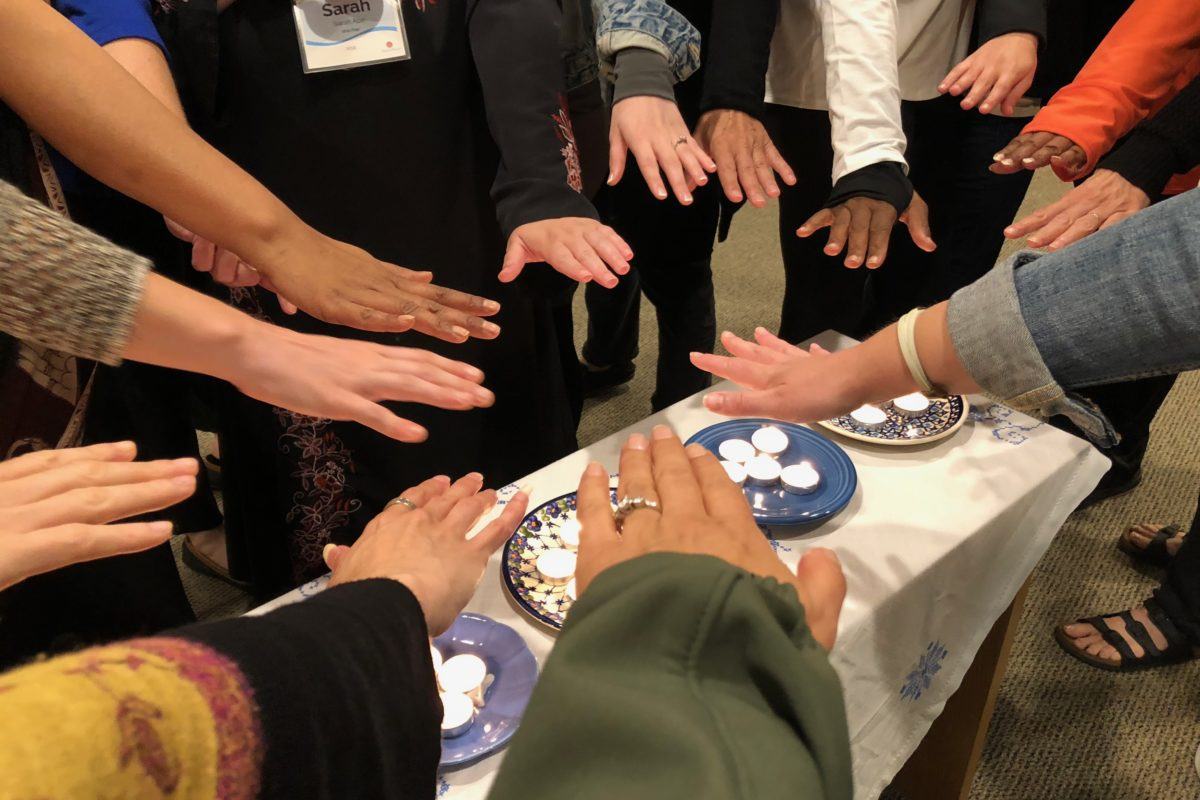 Photograph of 15 diverse women's hands stretched out toward each other in a circle.