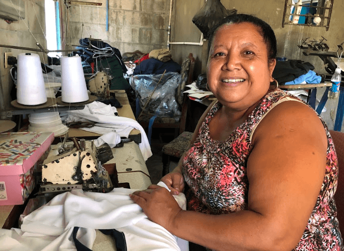 Photo of woman sitting at sewing machine showing her seamstress shop in El Salvador.