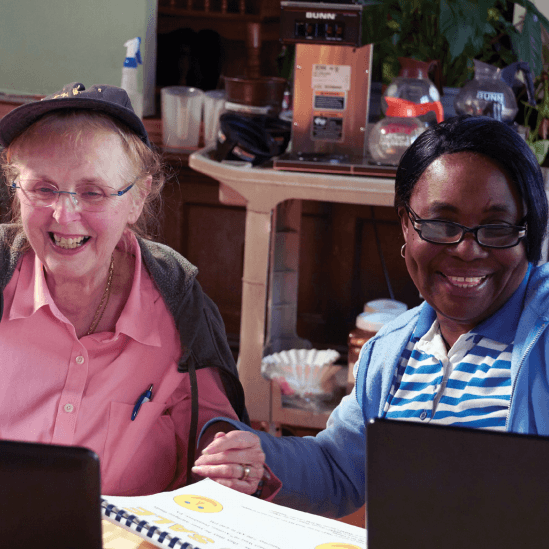 Adult student and teacher smiling in front of their computers.