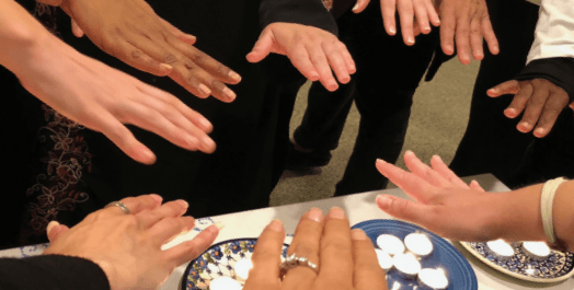 Multicolored hands extending blessing over votive candles.