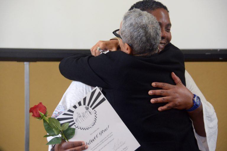 Two Black women hug while one of them receive a graduation diploma